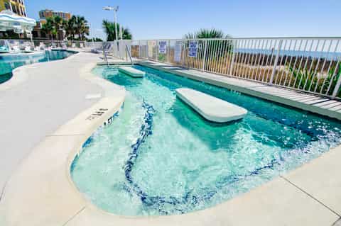 Oceanfront spa pool with jets and shallow water features, loungers, and water views beyond white railing