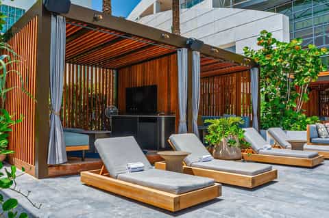 Luxury cabanas with wooden lounge chairs, pergolas, curtains, plants, and modern architecture