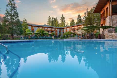 Large outdoor pool at mountain resort surrounded by evergreen trees at sunset with hotel in background