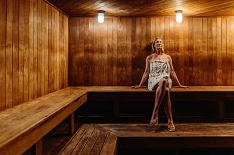 Woman relaxing on wooden bench in traditional sauna with wood paneling