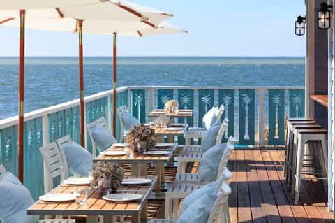 Oceanfront restaurant deck with dining tables, blue palm-patterned railing, and turquoise water view