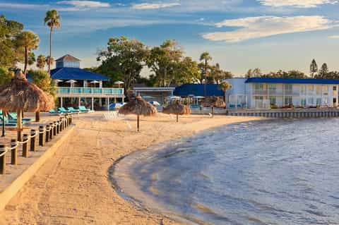 Beachfront resort with blue-roofed buildings, tiki umbrellas, and sandy shore at sunset