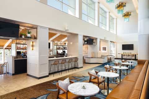 Bright hotel lobby with high ceilings, bar area, lounge seating, and blue patterned rug