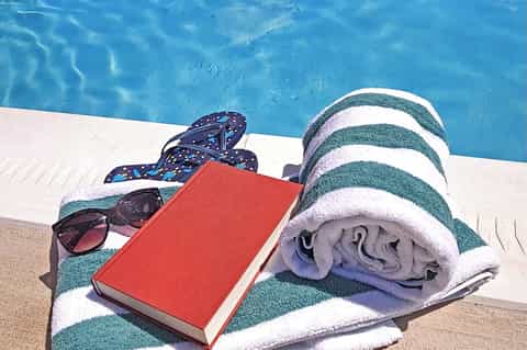 Poolside relaxation items including striped towel, sunglasses, flip-flops, and book by blue water