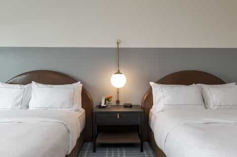 Guest room with two queen beds, brown leather headboards, pendant lighting, and minimalist décor