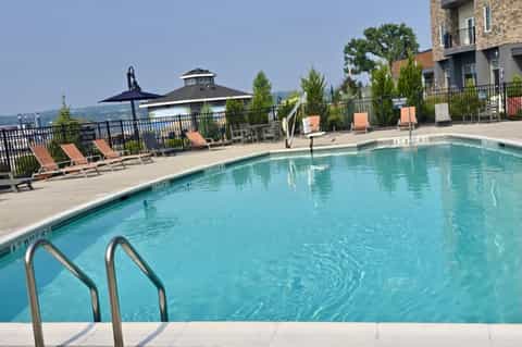Resort pool with turquoise water, lounge chairs, black umbrella, fencing, and multi-story buildings