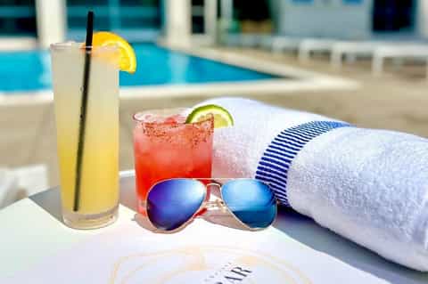 Poolside cocktails with citrus garnishes, sunglasses, towel, and blurred pool area in background
