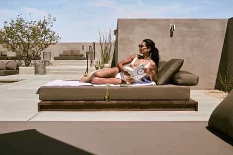 Woman relaxing on olive-green lounge chair on rooftop terrace with minimalist concrete design