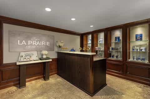 Luxury spa reception area with La Prairie branding, dark wood cabinetry, and glass display shelves