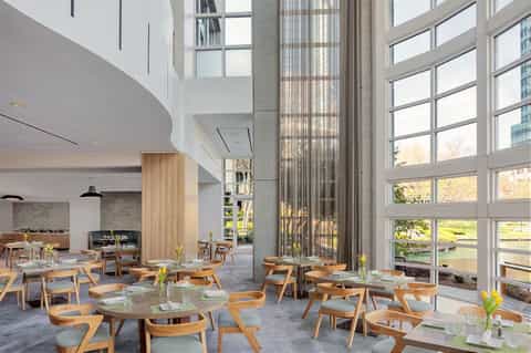 Modern restaurant dining room with high ceilings, wooden furniture, and large waterfront windows