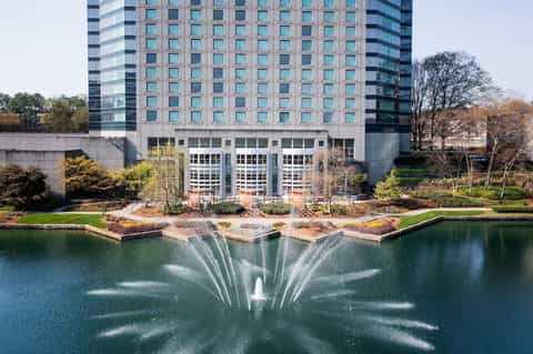 Modern high-rise hotel building with decorative fountain display in pond and manicured landscaping