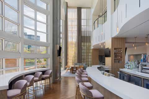 Modern hotel bar with high ceiling, floor-to-ceiling windows, and curved bar seating