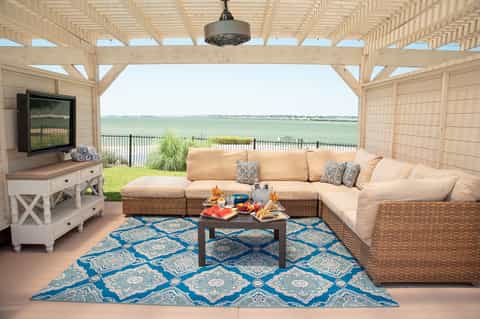 Beachfront pergola lounge with rattan seating, blue rug, and water views