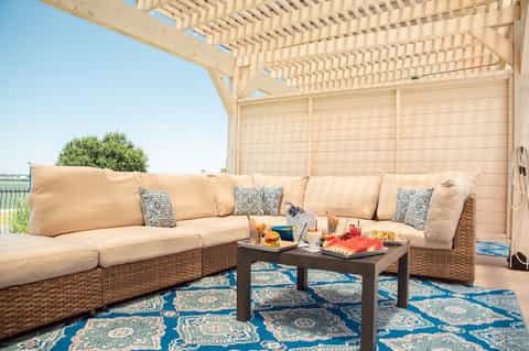 Upscale outdoor patio with wicker sectional sofa, pergola shade structure, and patterned rug