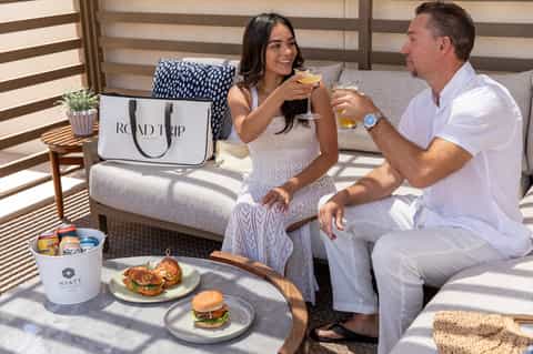 Couple enjoying drinks and appetizers on balcony with ocean view and Hyatt resort signage visible