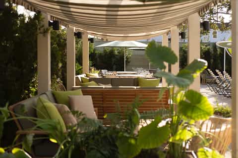 Shaded outdoor lounge area with striped awning, wooden seating, and views through palm trees and greenery
