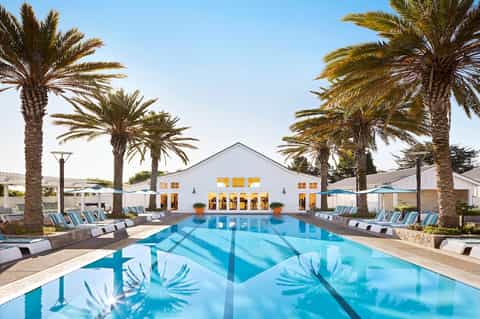 Resort lap pool with palm trees, white clubhouse building, and lounge chairs
