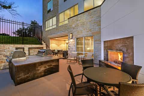 Twilight patio with outdoor fireplace, built-in grill station, dining area, stone construction, and illuminated windows
