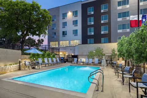 Contemporary hotel courtyard pool surrounded by multi-story building with blue loungers and seating