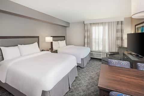 Hotel room with two queen beds, neutral décor, TV, and seating area