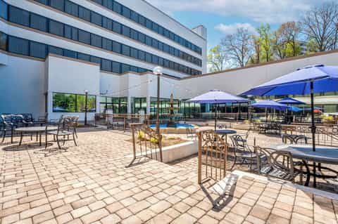 Hotel courtyard pool area with loungers, blue umbrellas, seating areas, and modern building facade