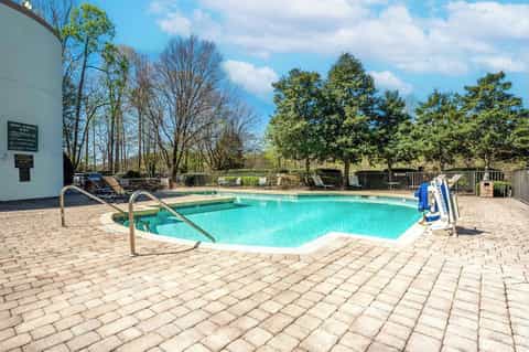 Community pool with turquoise water, metal railings, lounge chairs, and wooded surroundings