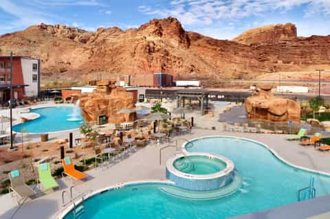 Resort pools with hot tubs, colorful loungers, dramatic red rock formations, and desert landscape