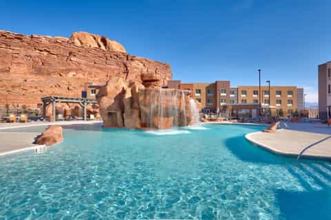 Resort pool with large rock waterfall feature, turquoise water, and modern hotel building