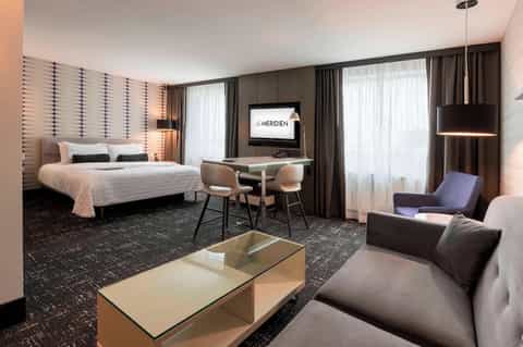 Contemporary hotel suite bedroom with accent wall, desk, and modern décor