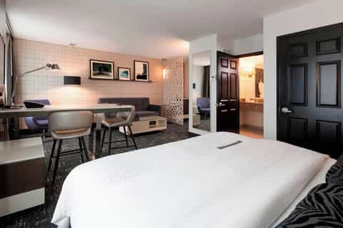 Modern hotel guest room with king bed, lounge area, tiled wall, and black doors