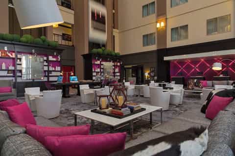 Hotel lobby lounge with modern design, magenta accents, white seating, and indoor plants