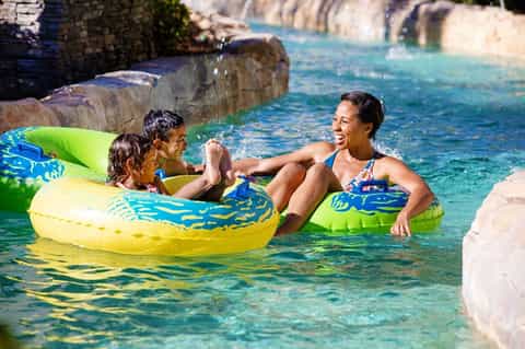 Family enjoying colorful inflatable floats in clear turquoise water surrounded by stone walls