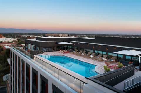 Rooftop hotel pool at dusk with city skyline views, loungers, and modern architectural design