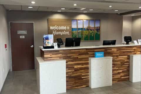 Hotel reception desk with wooden accent wall, welcome signage, Hilton branding, and check-in counter