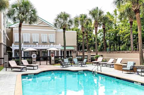 Resort pool surrounded by lounge chairs, umbrellas, palm trees, and poolside bar