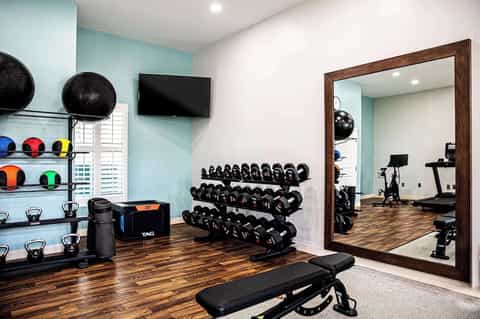Modern fitness center with dumbbell rack, exercise bikes, black medicine balls, and large mirror