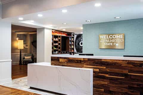 Hotel check-in desk with marble counter, teal accent wall, and welcome signage