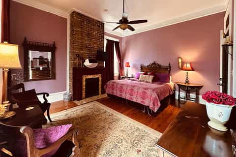 Elegant bedroom with mauve walls, fireplace, ornate wooden bed, and decorative furnishings
