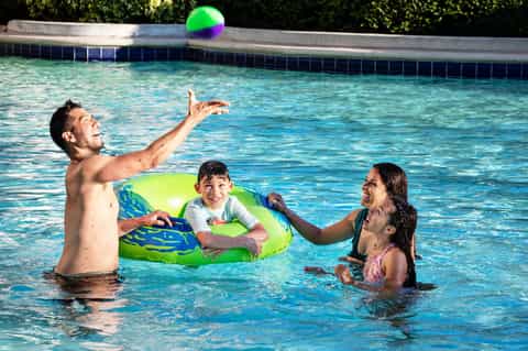 Family playing with colorful ball in resort pool during daytime