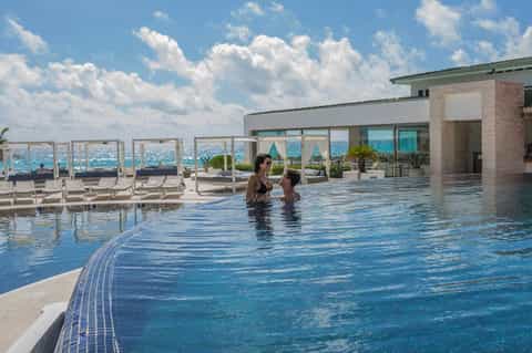 Resort infinity pool with ocean views, guests swimming, loungers, and modern coastal architecture