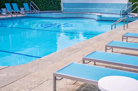 Resort lap pool with blue lounge chairs, ivy-covered walls, and geometric pattern deck