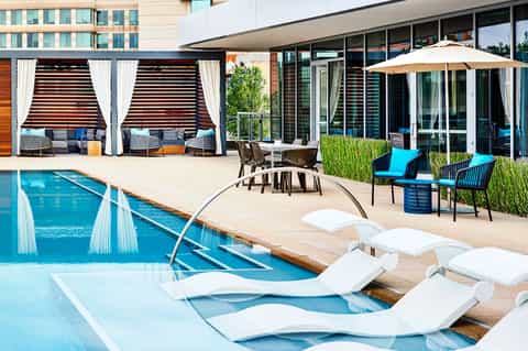 Luxury resort pool deck with white lounge chairs, cabanas with curtains, and modern building architecture