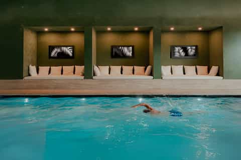 Indoor lap pool with three alcove seating areas featuring cream cushioned benches and green accent walls