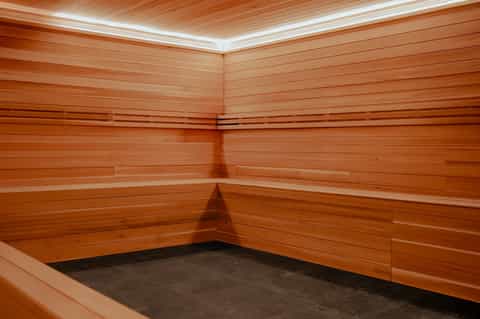Empty wooden sauna room with corner bench seating and ambient lighting