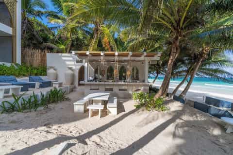 Beachfront cabana with white pergola, ocean view, coconut palms, and sand