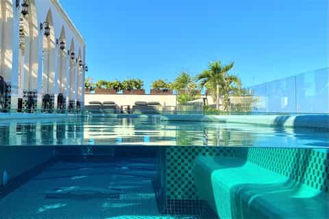 Indoor lap pool with underwater viewing window, architectural columns, and palm trees
