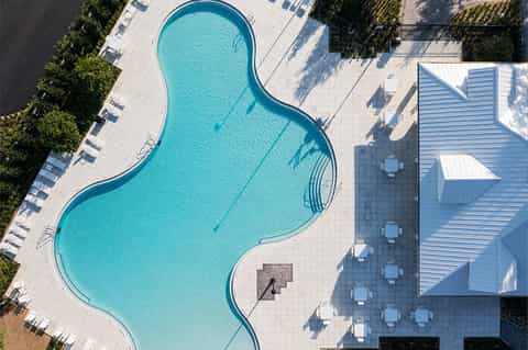 Resort pool with curved shape, white lounge chairs, modern architecture, and landscaped grounds from aerial view