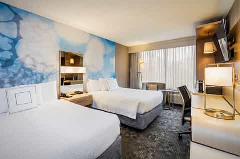 Hotel guest room with two queen beds, desk, armchair, and blue water-themed wall art