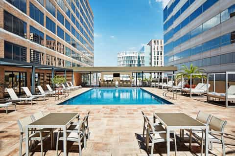 Rectangular outdoor pool surrounded by lounge chairs and modern high-rise buildings
