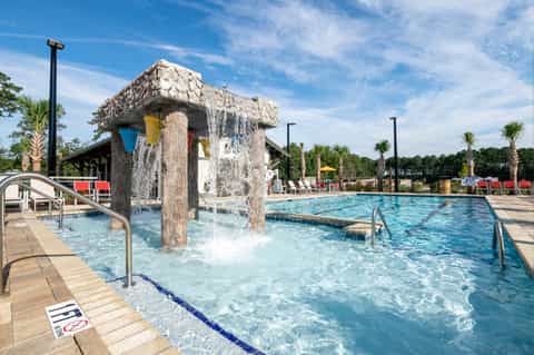 Outdoor resort swimming pool with wooden bucket water feature and palm trees under clear blue sky